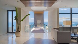 Un moderno vestíbulo de hotel con barandilla de vidrio, un mostrador de recepción y una planta grande en maceta.