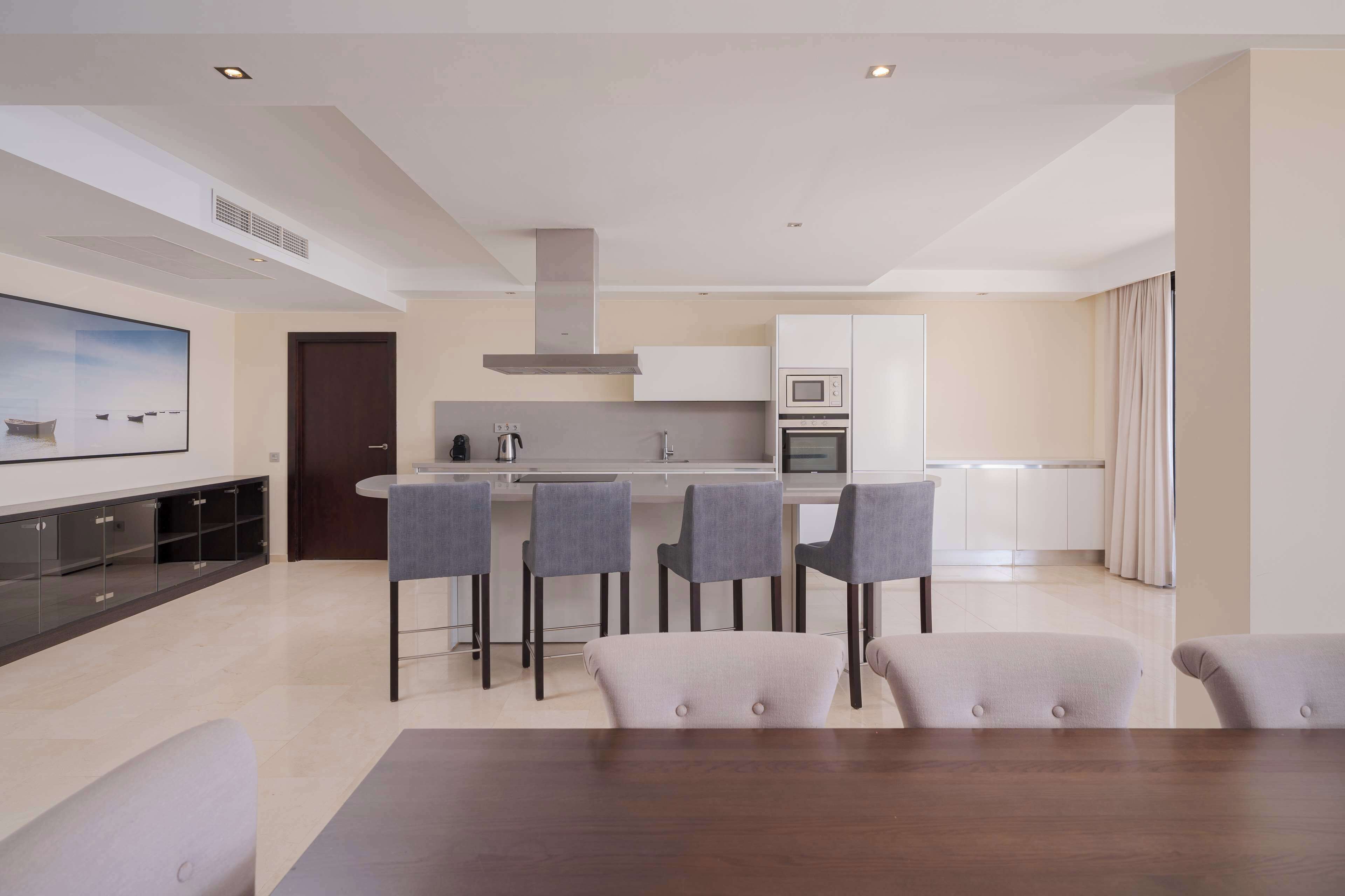 Una cocina moderna con una isla central, taburetes de bar y un comedor con mesa y sillas.