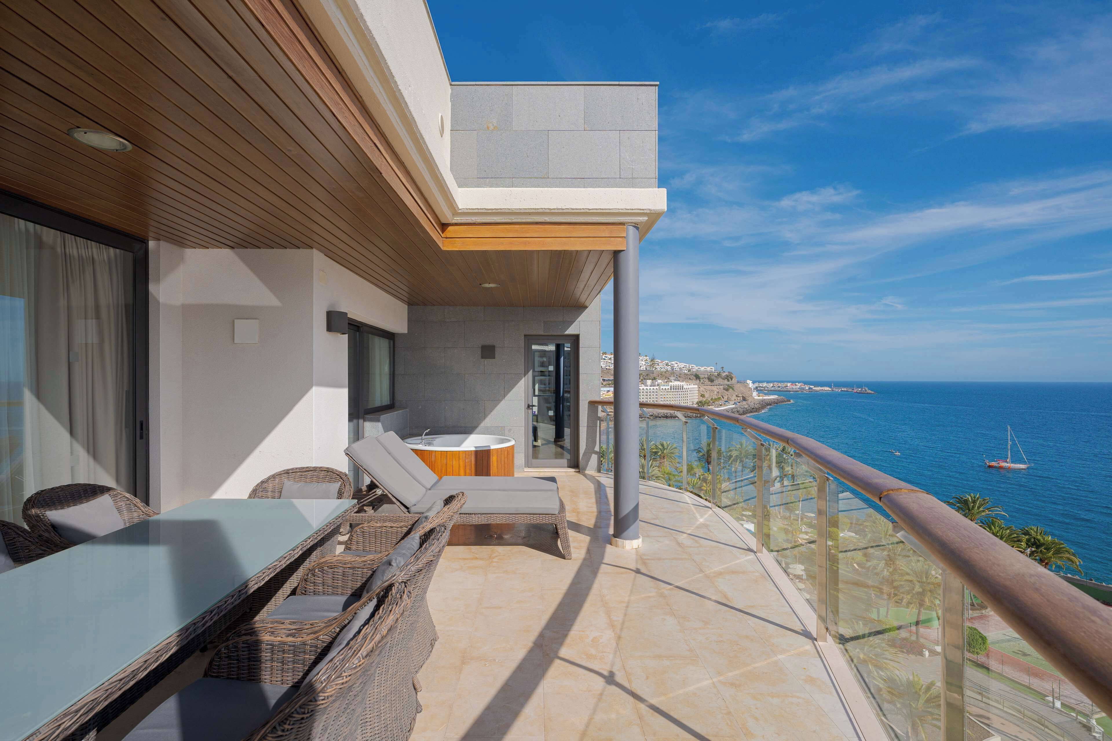A balcony with a view of the sea, wicker furniture, and a glass railing.