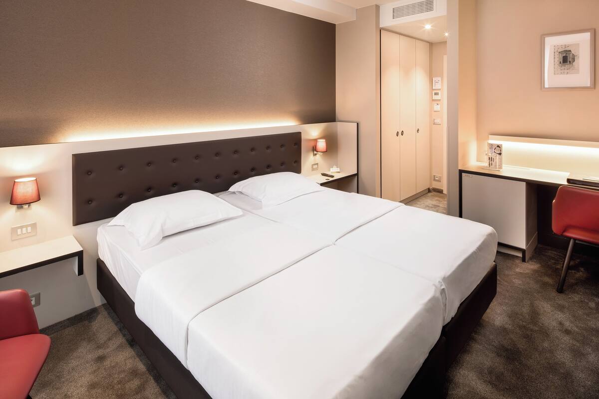 Hotellihuone, jossa on suuri sänky, yöpöydät valaisimineen, työpöytä ja tuoli.