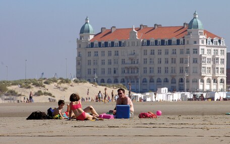 A beach with people and a large historic building with domed roofs in the background.