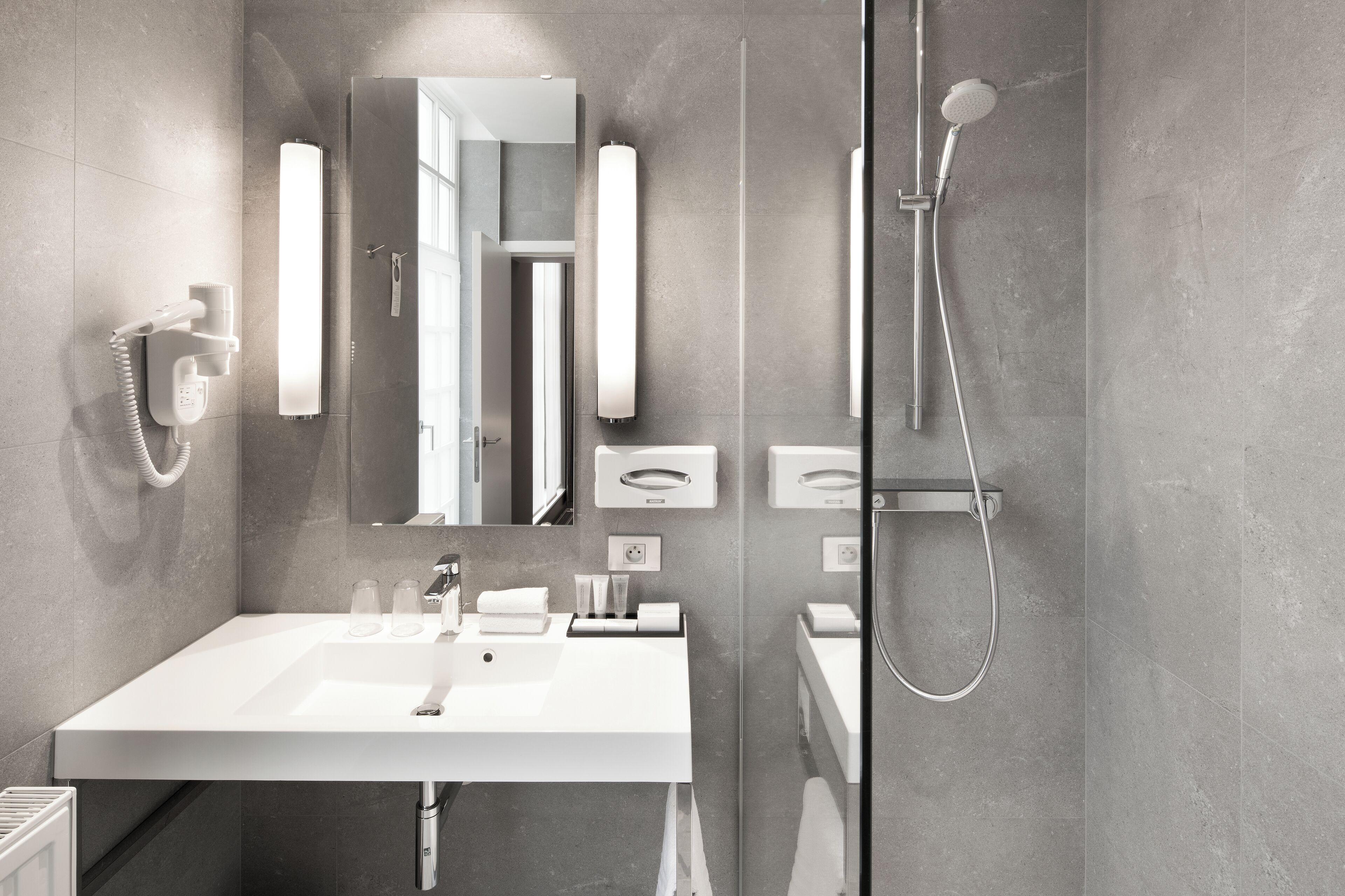 A modern bathroom with a large mirror, a white sink, a handheld showerhead, and a towel rack.