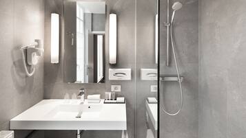 Une salle de bain moderne avec un grand miroir, un lavabo blanc, une douchette à main et un porte-serviettes.