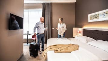 Ein Hotelzimmer mit Bett, Fernseher, Schreibtisch und einem Fenster mit Vorhängen.