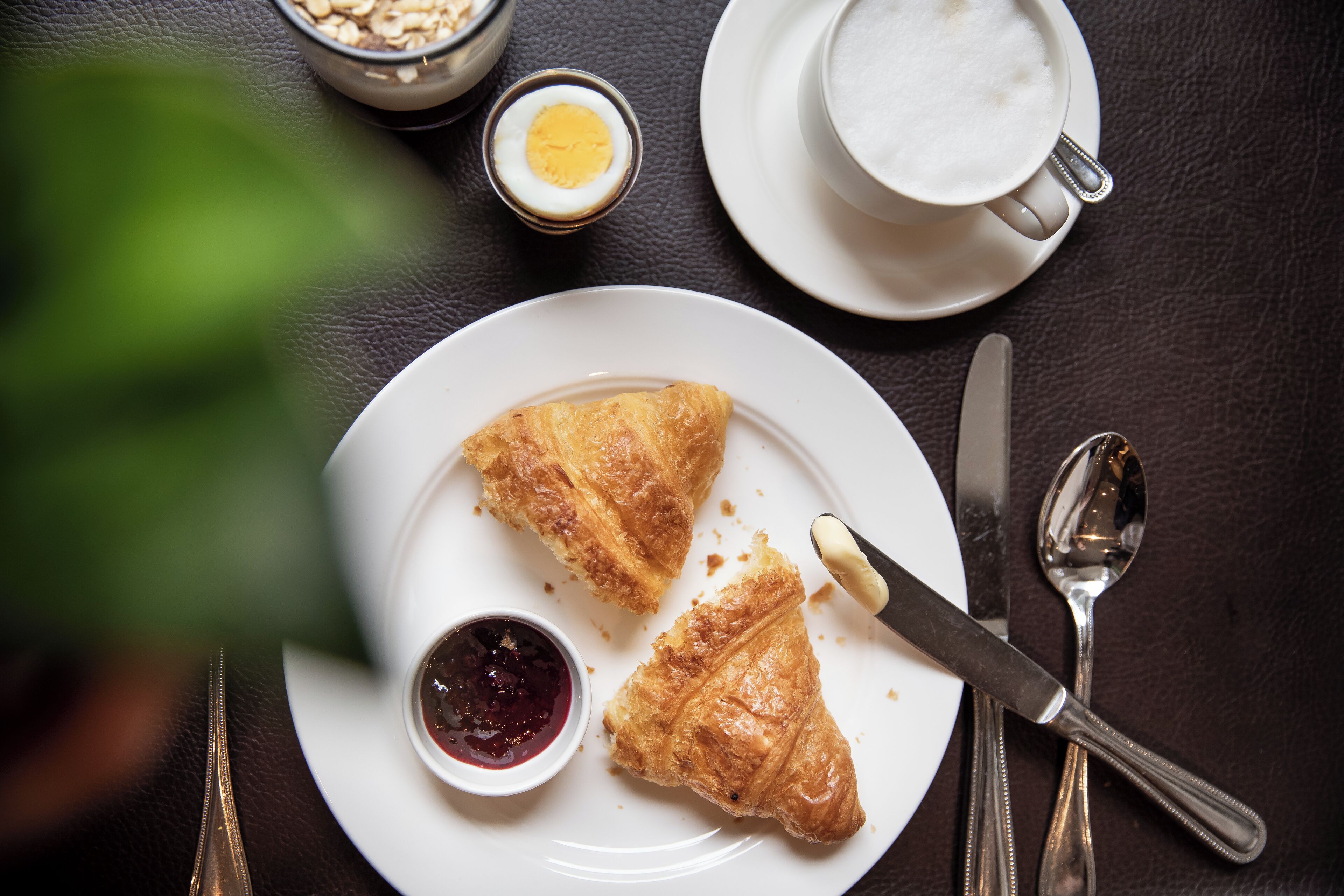 Un plat amb croissants i un bol petit de melmelada, una tassa de cafè i un bol de porridge sobre una taula fosca.