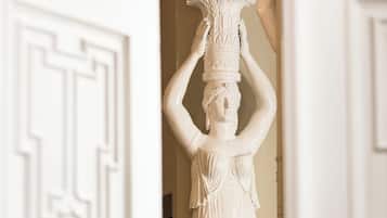 Eine weiße Statue einer Frau, die eine Schale auf dem Kopf balanciert, steht in einer Türöffnung mit dekorativem Türrahmen.