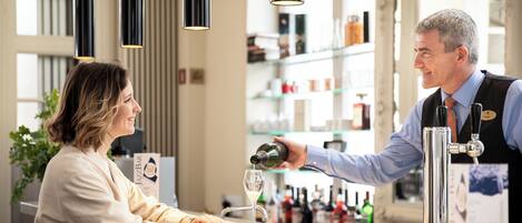 A bar area with a bartender pouring a drink into a glass. There are shelves with bottles in the background.