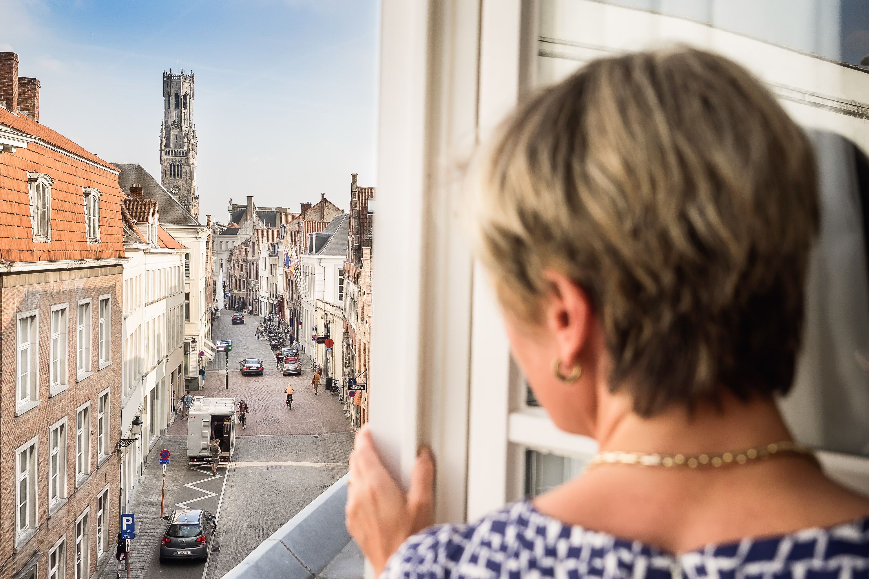 A view from a window overlooking a street with buildings and a tower.