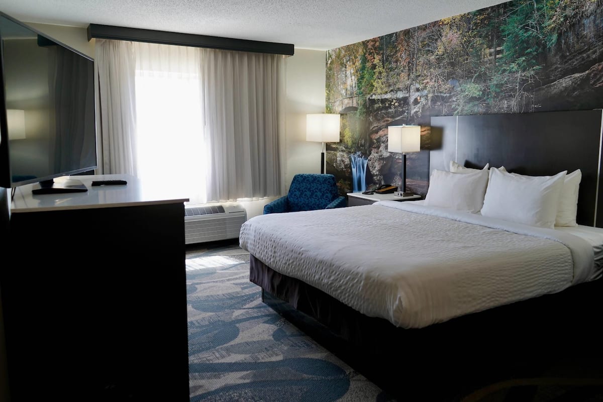 A hotel room with a large bed, a desk with a computer, a chair, a TV, and a window with curtains.