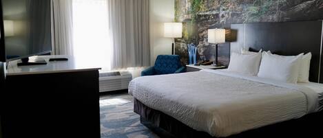 A hotel room with a large bed, a desk with a computer, a chair, a TV, and a window with curtains.