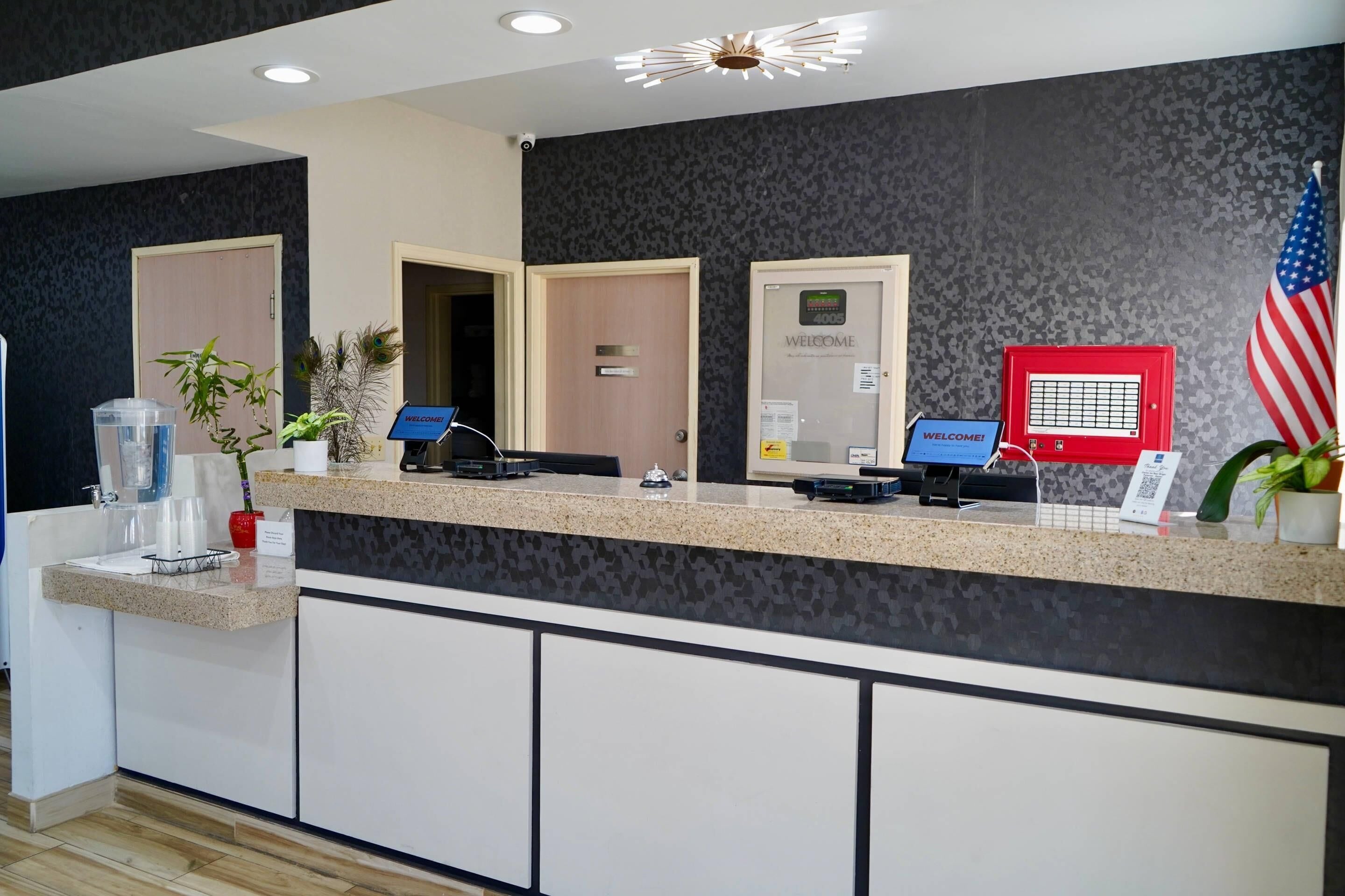 A reception desk with a computer, a 'WELCOME!' sign, an American flag, and a door with a 'WELCOME' sign.