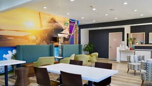 Un moderno vestíbulo de hotel con un mural grande, zonas de estar, un mostrador de recepción y una estación de café.