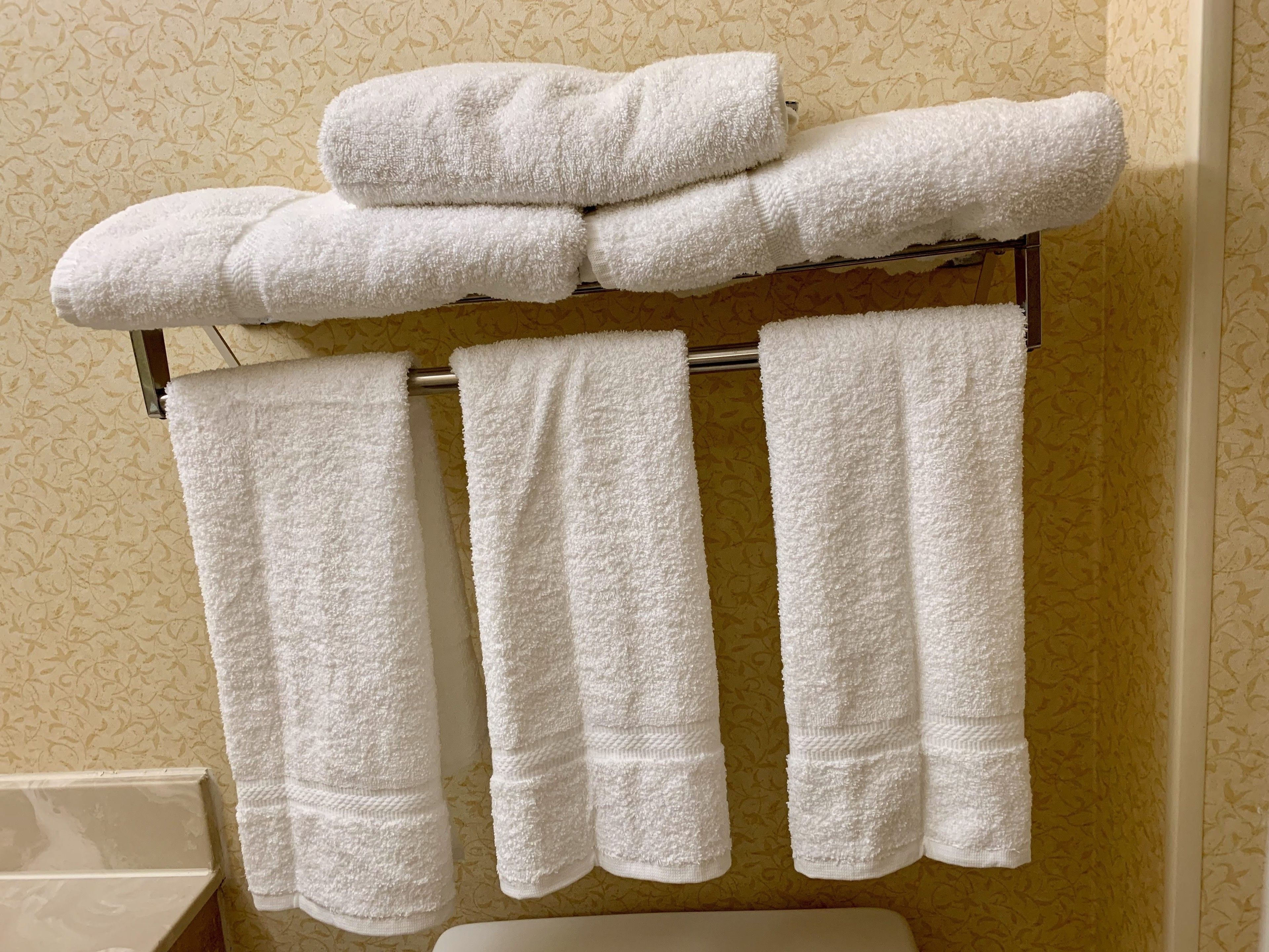 A bathroom with a towel rack holding four white towels.