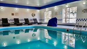 Piscina interior con sillones de descanso, zona cubierta y ventana con vista a un árbol.