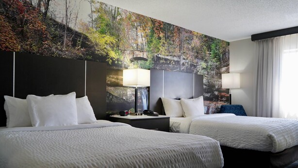 Una habitación de hotel con dos camas, un mural grande en la pared y una ventana con cortinas.