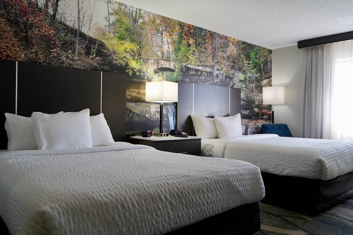A hotel room with two beds, a large wall mural, and a window with curtains.