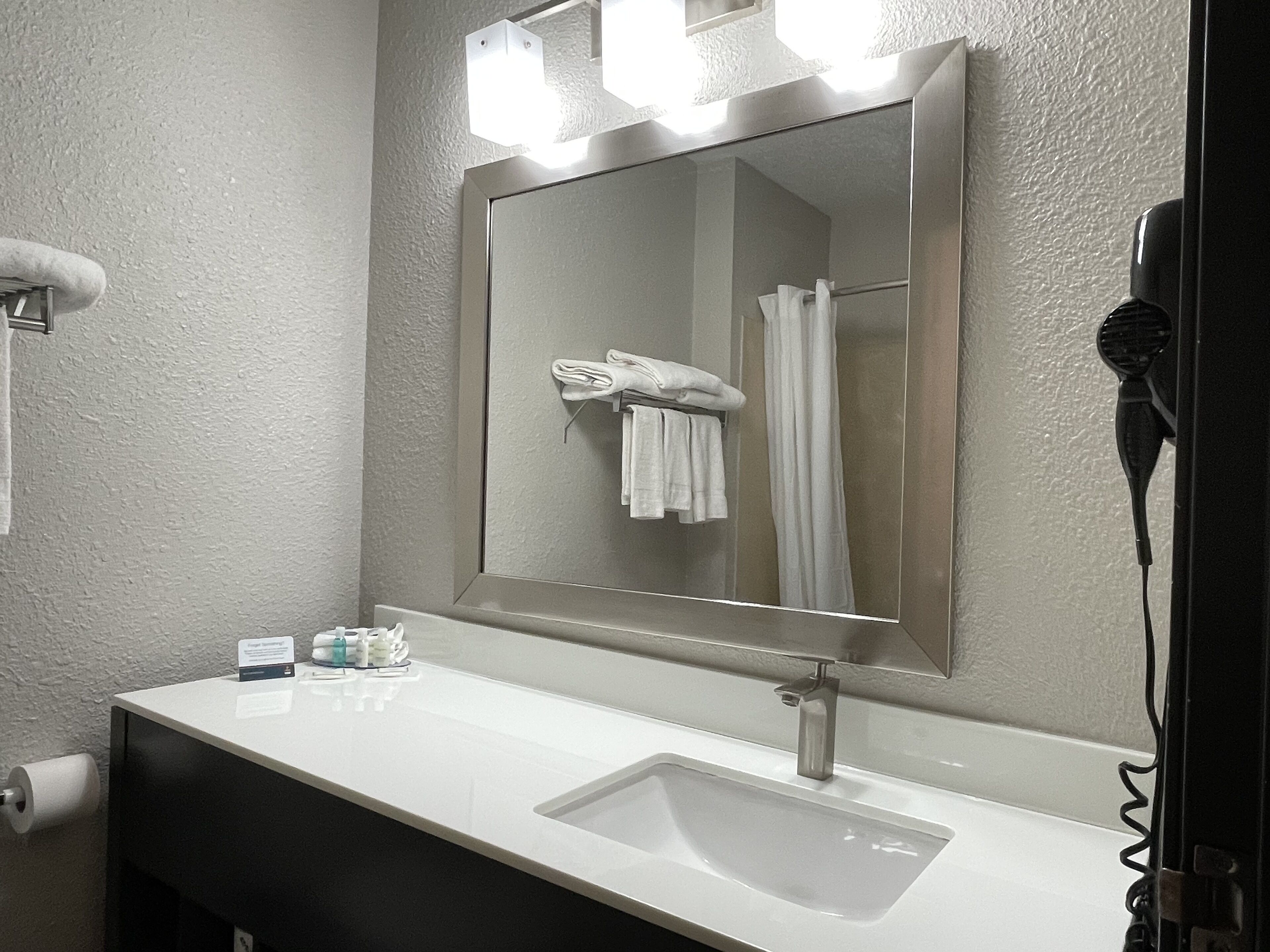Une salle de bain avec un lavabo blanc, un miroir et un sèche-cheveux.