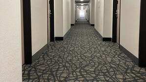Un pasillo de hotel con alfombra estampada, varias puertas y una lámpara en el techo.