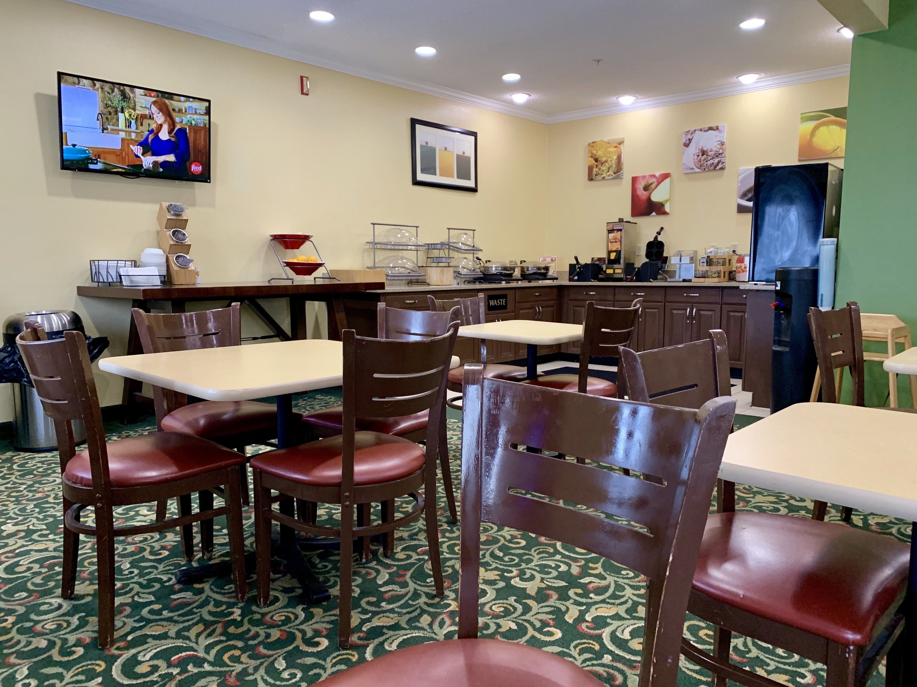 Un restaurant amb diverses taules i cadires, un televisor que mostra un programa de cuina, i diferents aparells de cuina i elements decoratius.