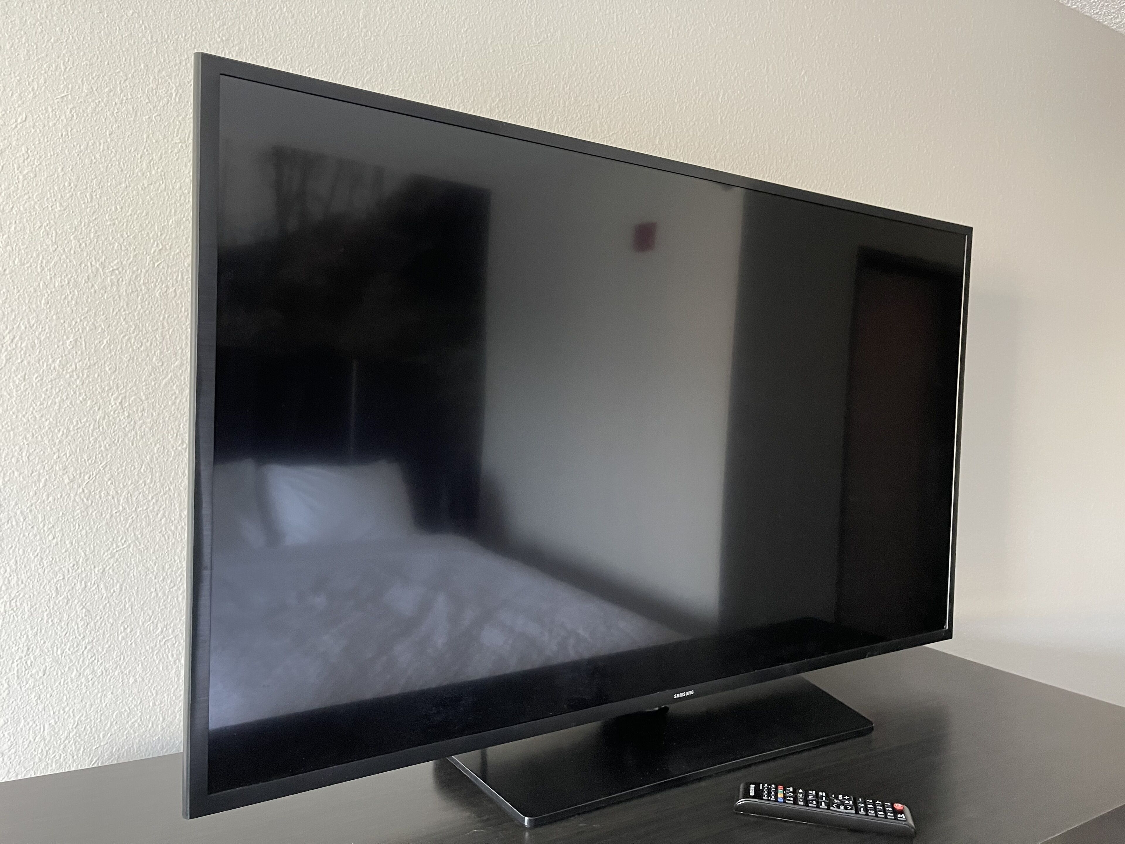 Ein Flachbildfernseher auf einem Ständer mit einer Fernbedienung auf einem Tisch.