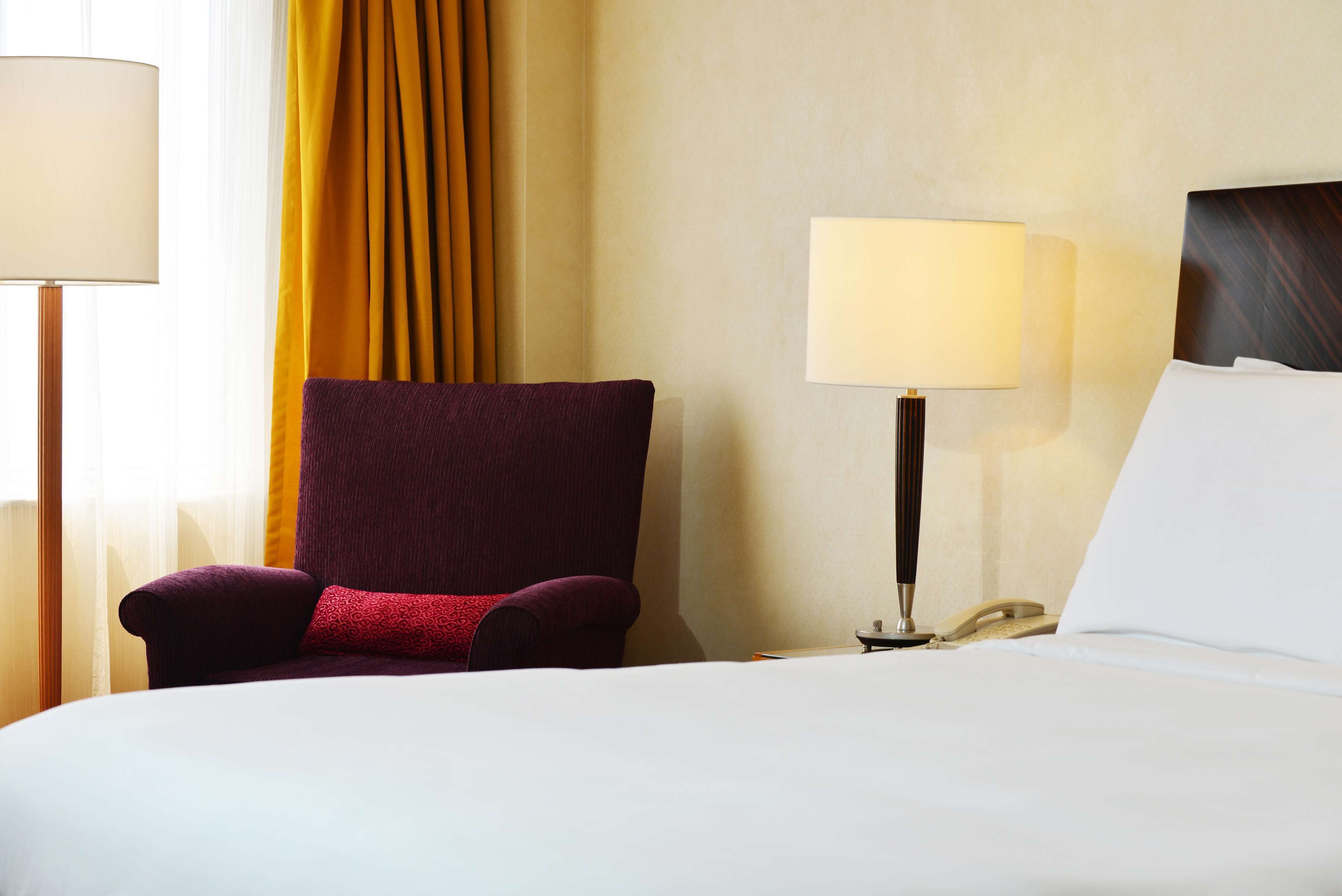 A hotel room with a bed, a chair, a lamp, and a telephone.
