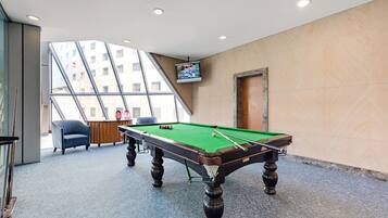 A pool table in a room with a large window, a chair, and a television on the wall.