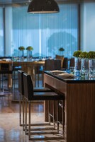A modern dining area with wooden tables, chairs, and tall vases with greenery.