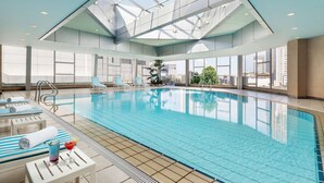 An indoor swimming pool with clear glass walls, lounge chairs, and a view of the city skyline. - Radisson Collection Yangtze Shanghai (Shanghai)