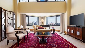 A spacious living room with a high ceiling, large windows offering a city view, a flat-screen TV, and a red patterned carpet. - Radisson Collection Yangtze Shanghai (Shanghai)