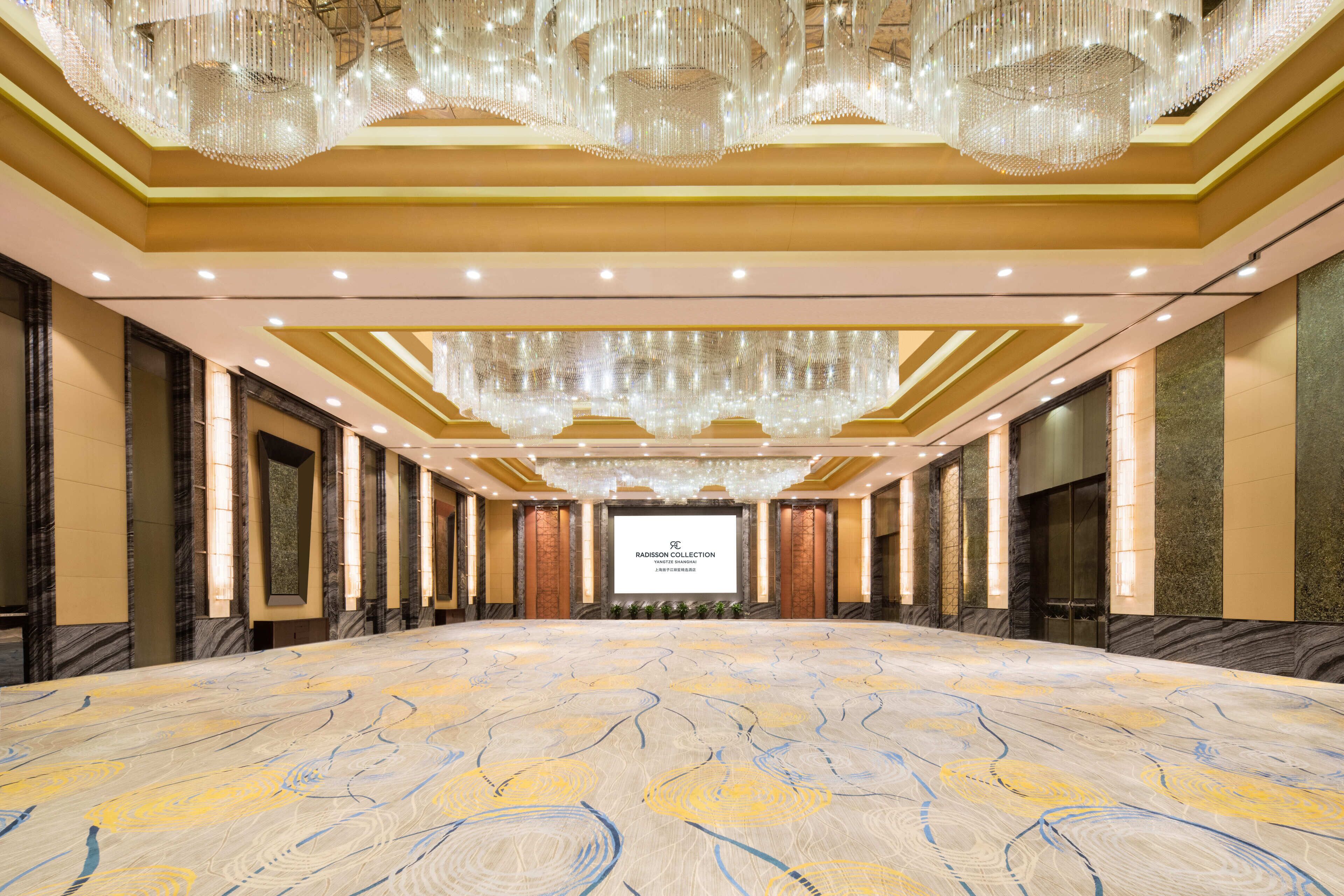 Una amplia sala de conferencias con un piso de diseño, una pantalla de proyección central y candelabros ornamentados.
