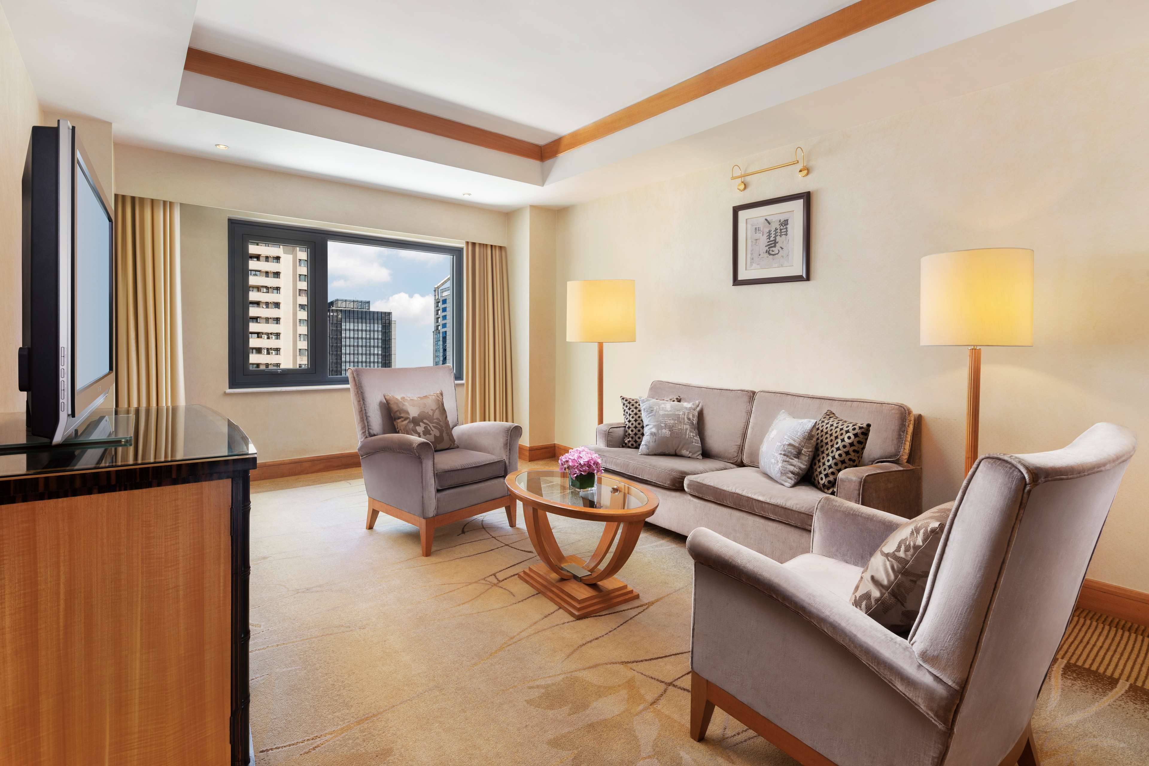 Een hotelkamer met een flatscreen televisie, twee fauteuils, een bank, een salontafel en twee vloerlampen.