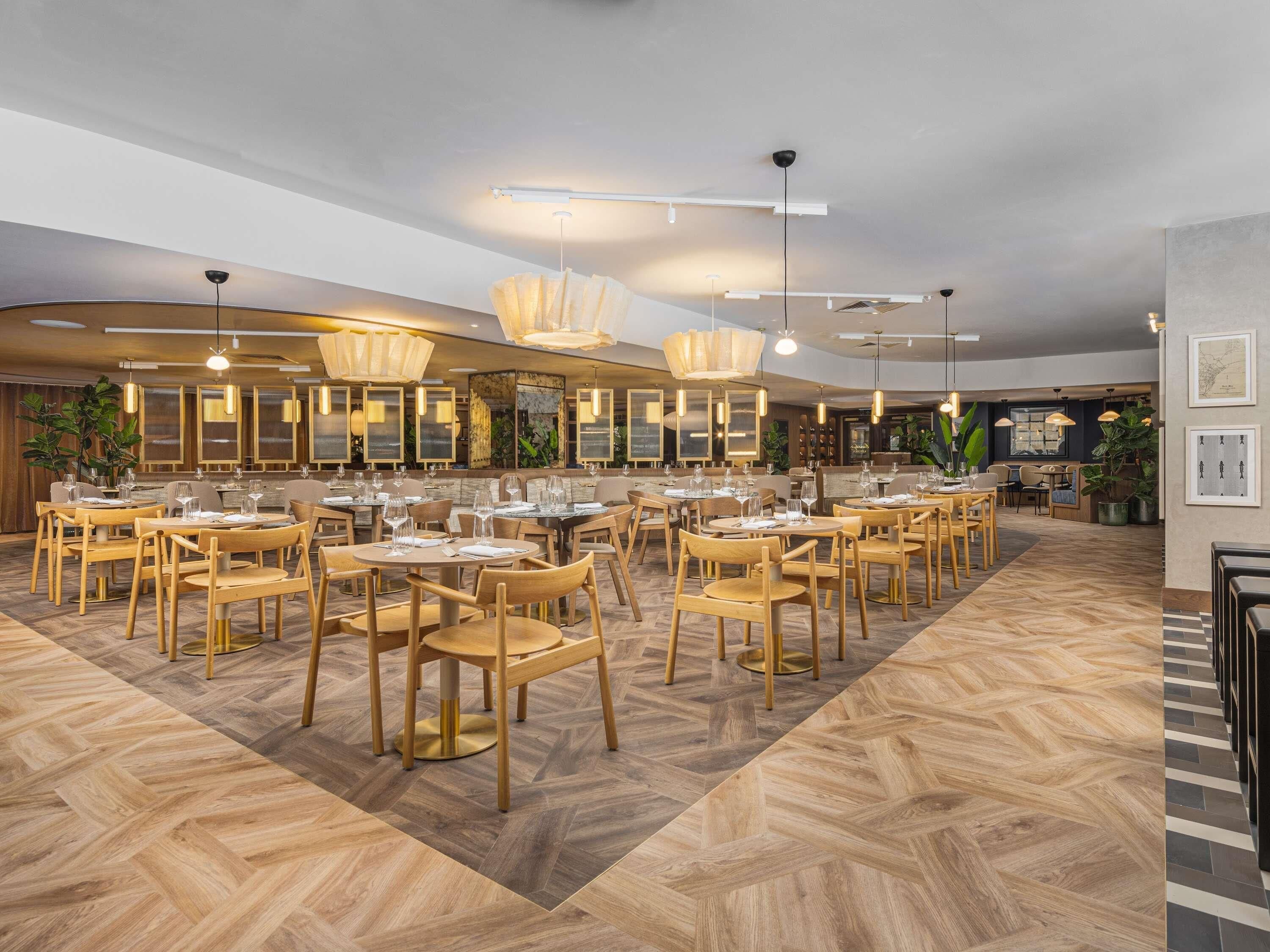 Un restaurante con mobiliario de madera, iluminación colgante y un patrón de suelo tipo espiga.