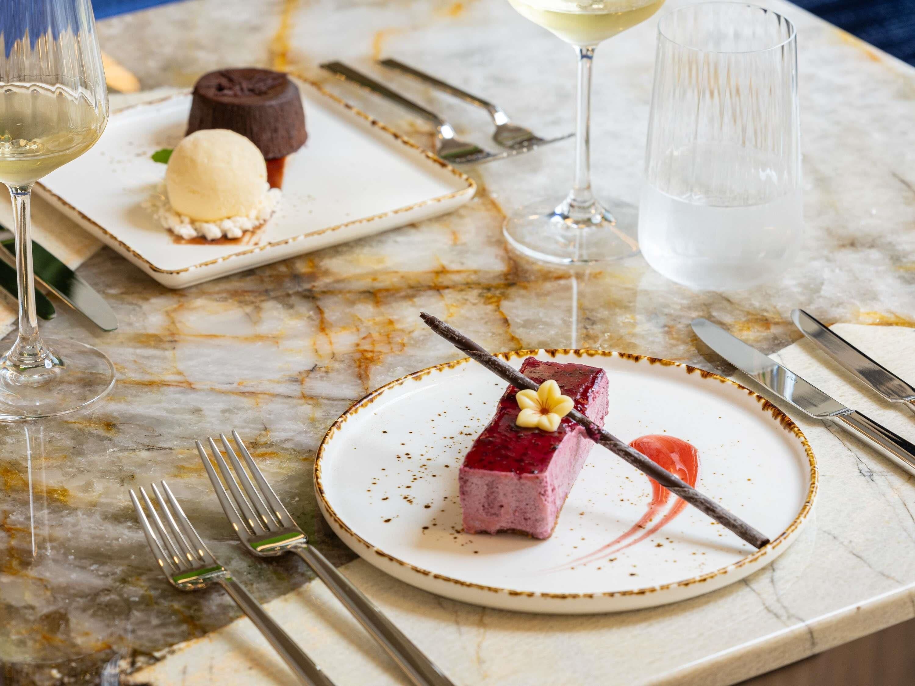 A marble table with a dessert plate, a glass of white wine, and a dessert with a cherry on top.