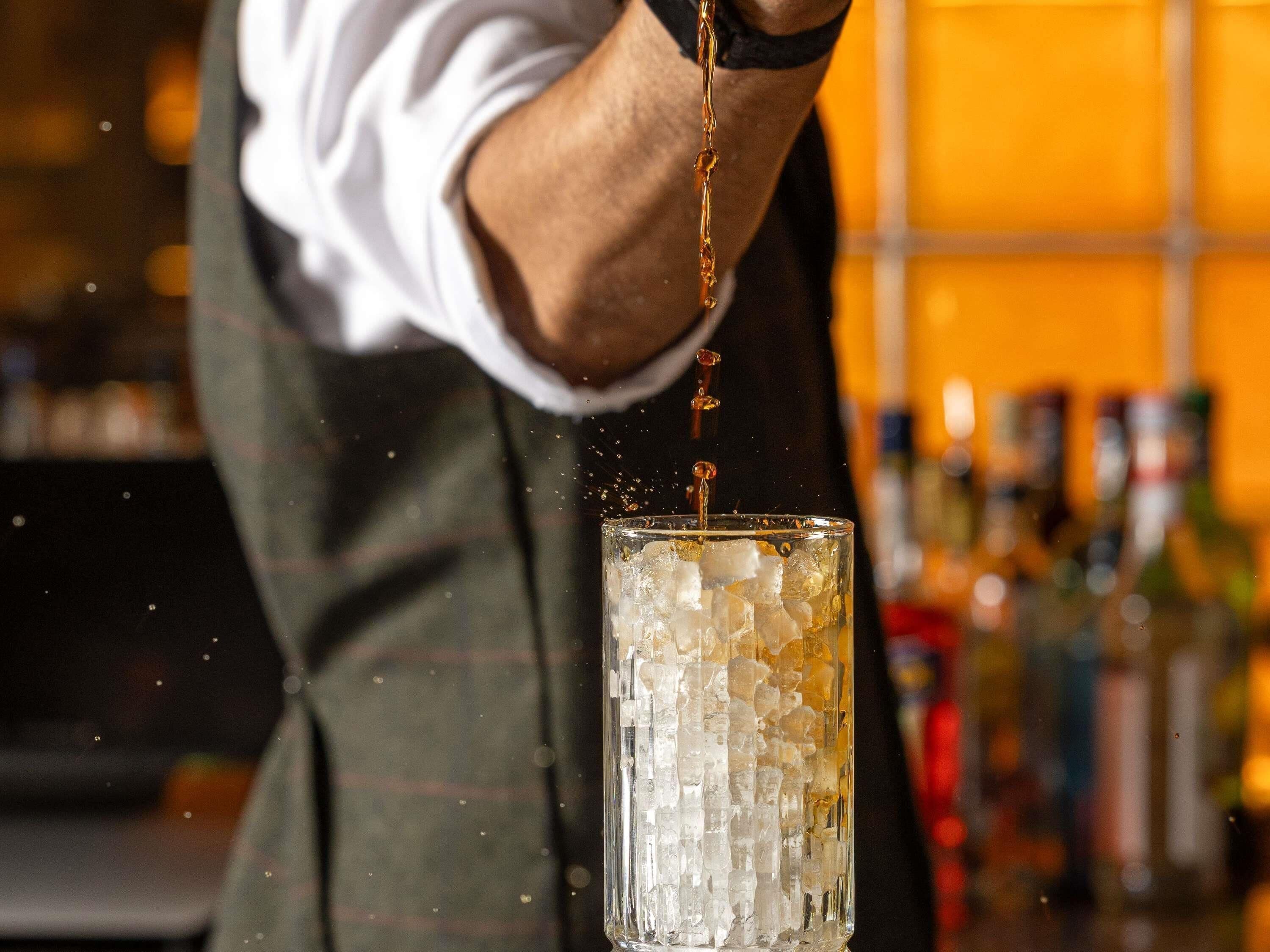 A bartender pouring a drink into a glass with ice.