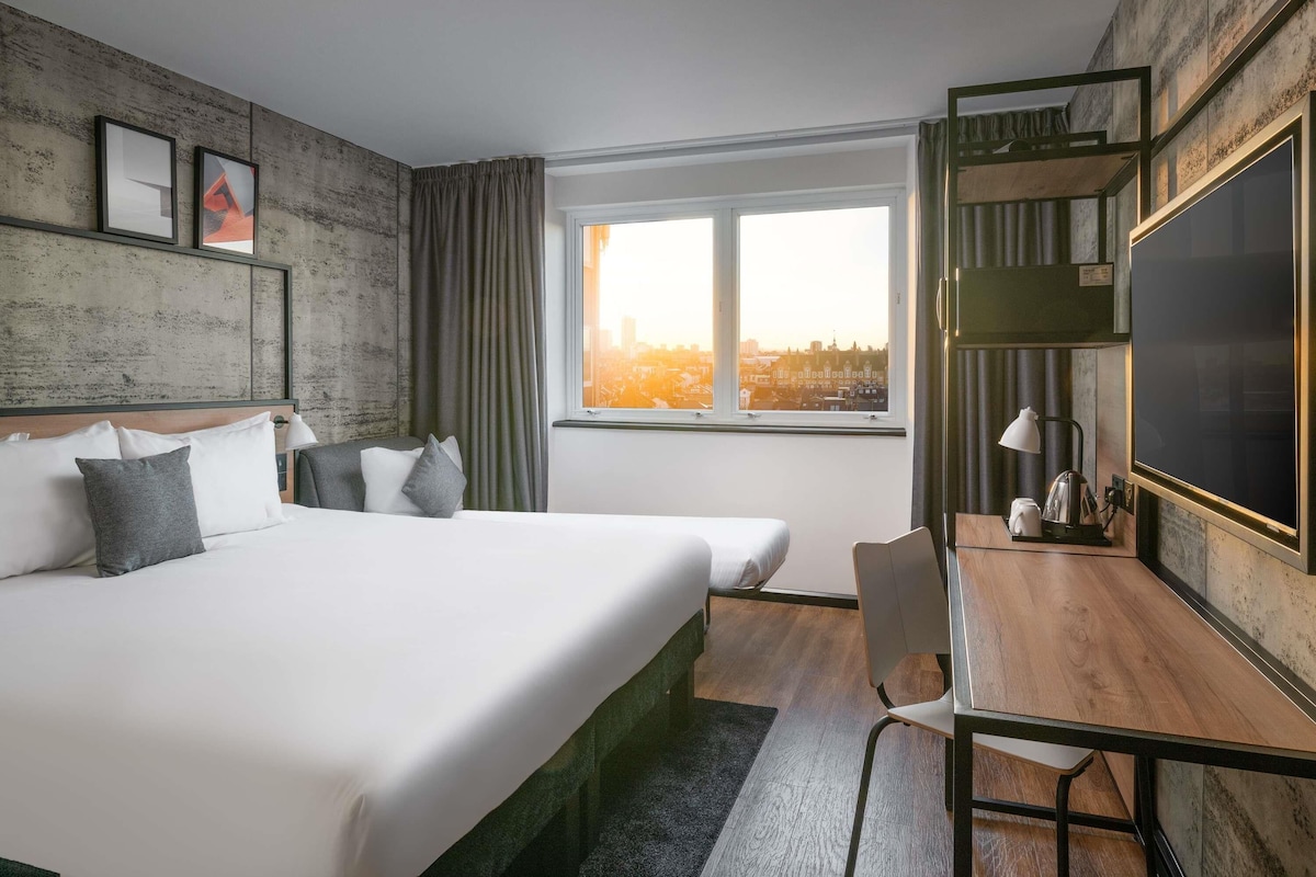 Une chambre d’hôtel dotée d’un grand lit, d’un bureau avec une chaise, d’une télévision à écran plat et d’une fenêtre donnant sur la ville.