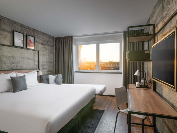 Quarto de hotel com uma cama grande, uma escrivaninha com cadeira, televisão de tela plana e janela com vista para a cidade.