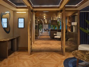 Een hotel lobby met een visgraat vloerpatroon, een receptiebalie en een zithoek met een ronde tafel.