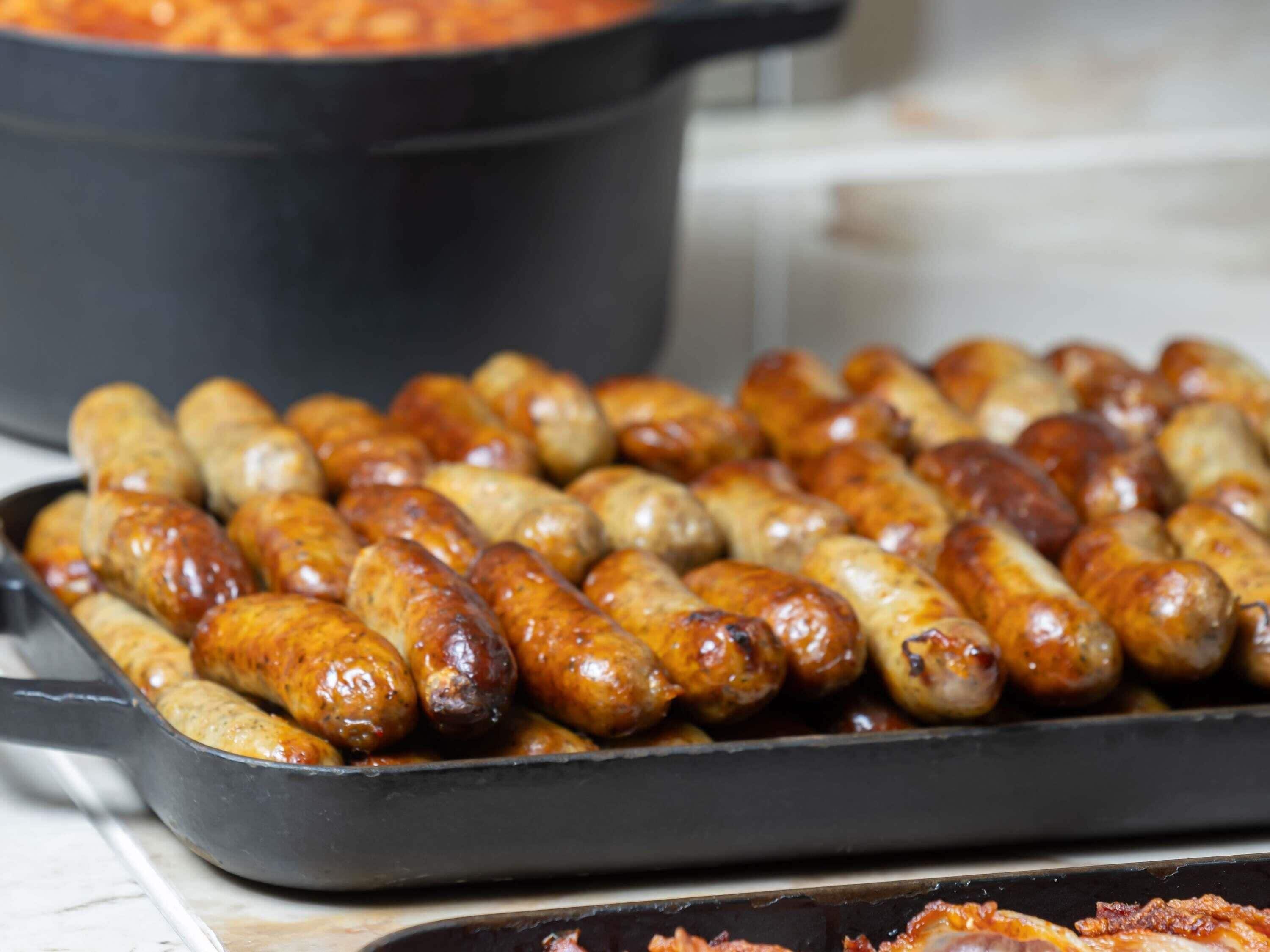 A tray of cooked sausages in a black pan.