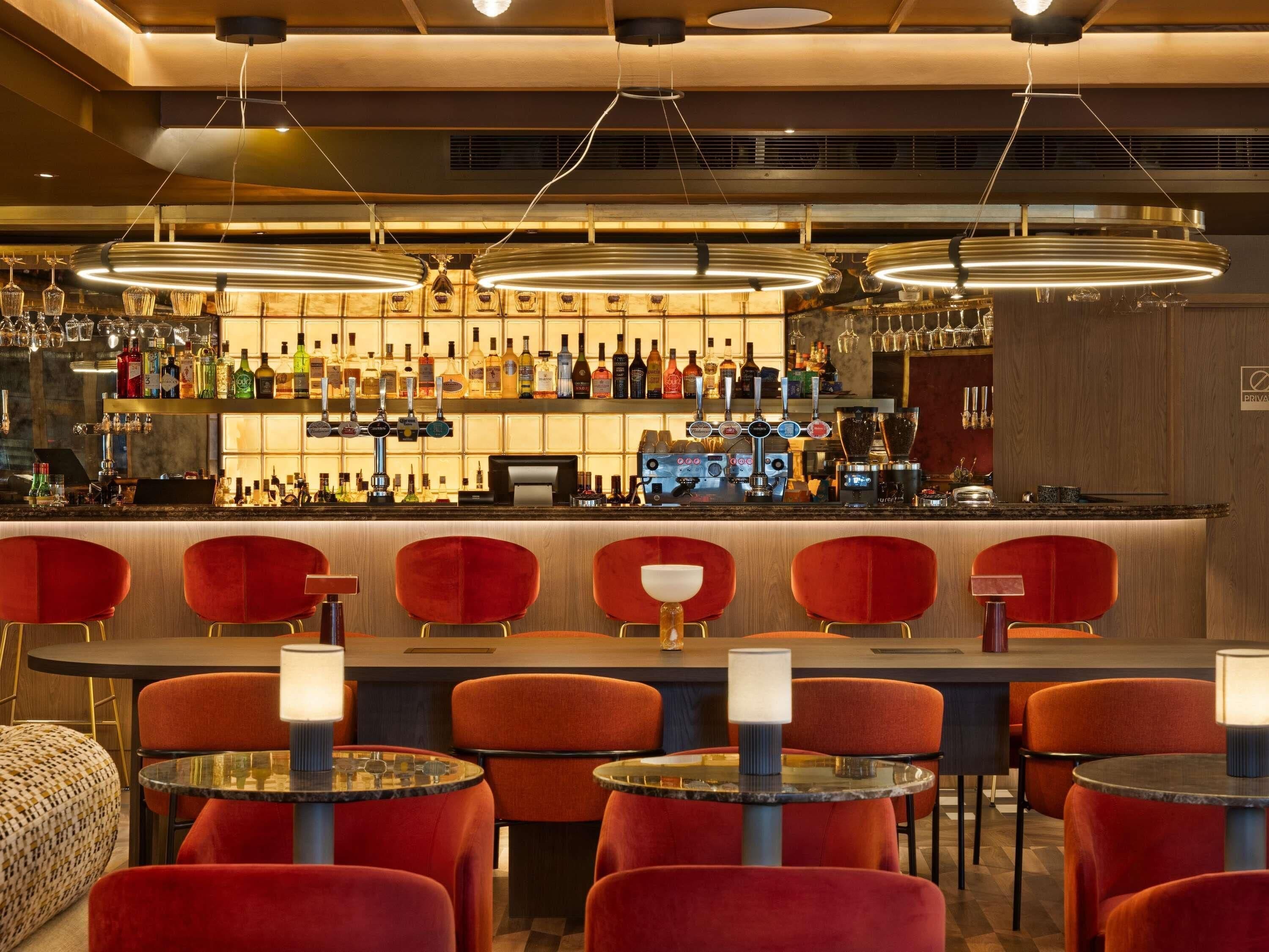 Un área de bar con diversas opciones de asientos, una barra bien surtida y luminarias colgantes.