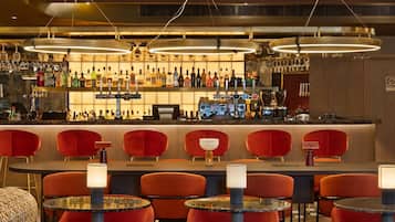 Un área de bar con diversas opciones de asientos, una barra bien surtida y luminarias colgantes.