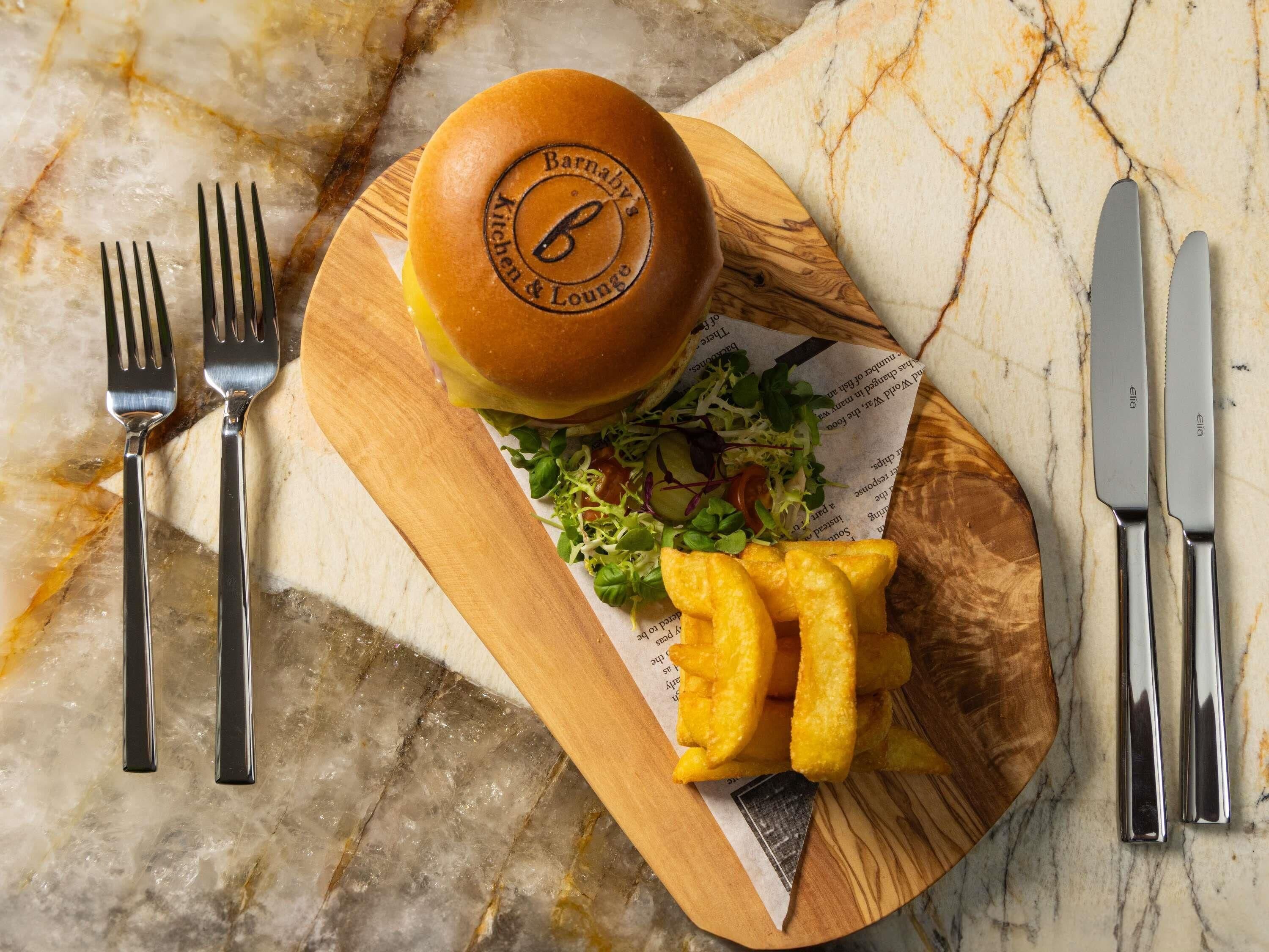 A meal on a wooden board with a burger, fries, and salad, accompanied by cutlery.