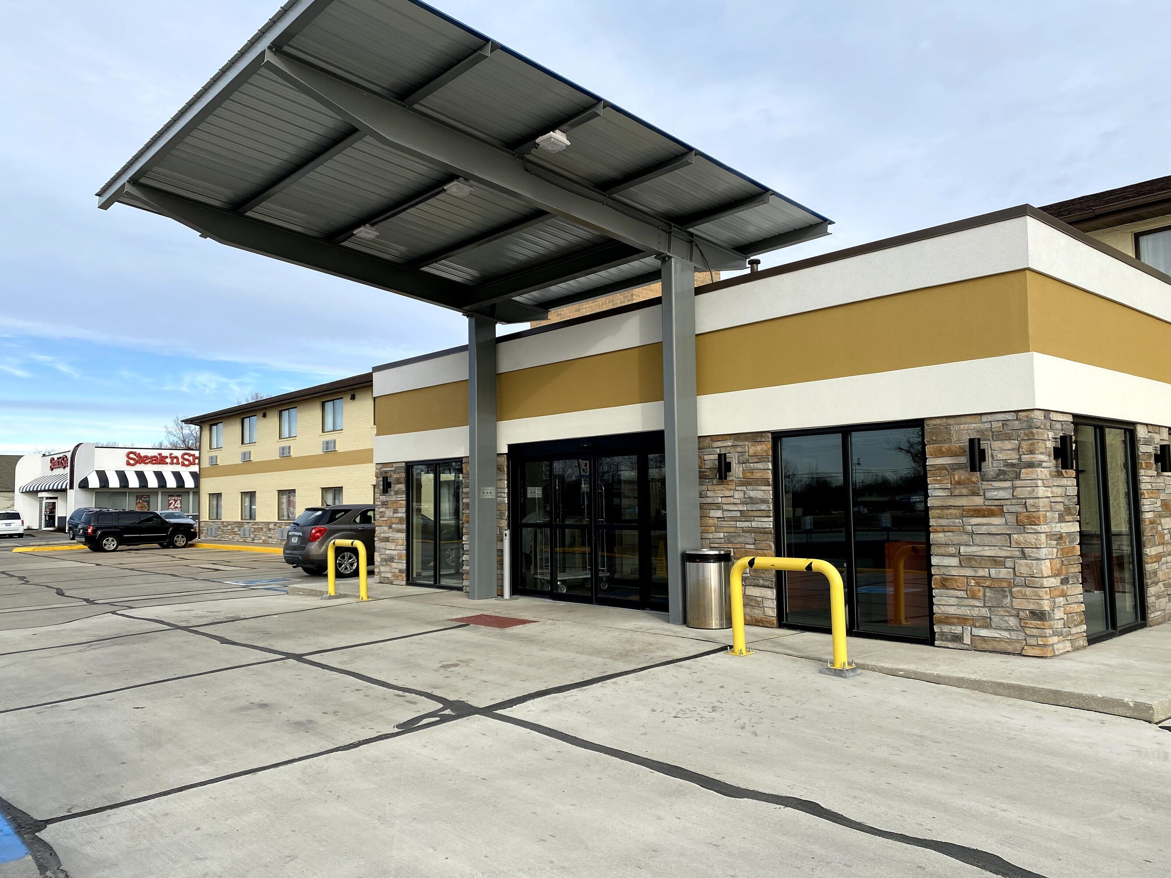 A building with a modern design, featuring a covered parking area and a storefront with a sign.