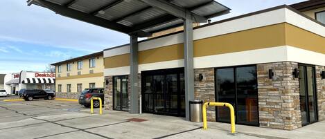 A building with a modern design, featuring a covered parking area and a storefront with a sign.