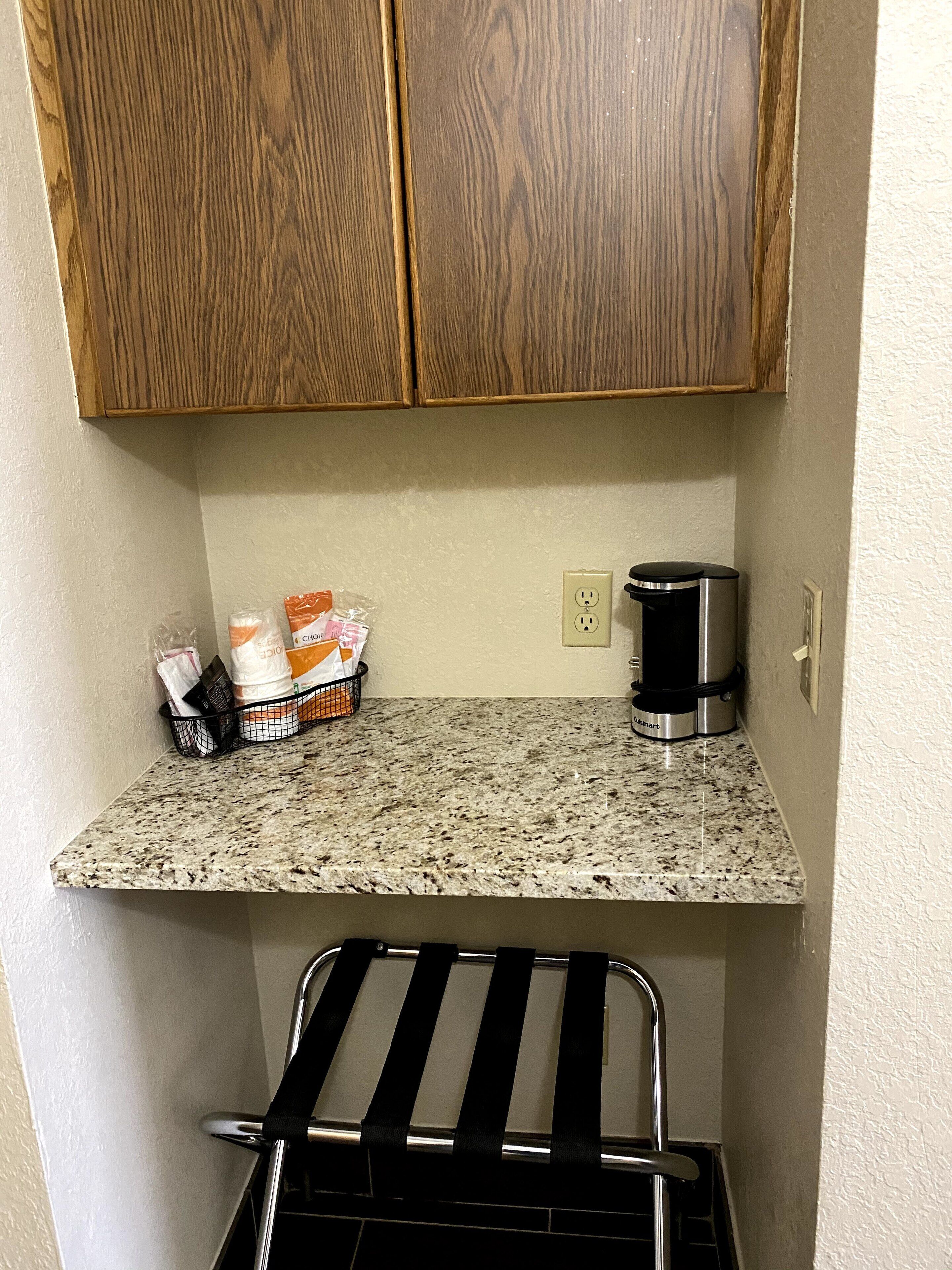 A kitchen with wooden cabinets, a granite countertop, a coffee maker, and a black metal rack.