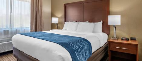 A hotel room with a large bed, two bedside lamps, a nightstand with a clock, and a window with sheer curtains.