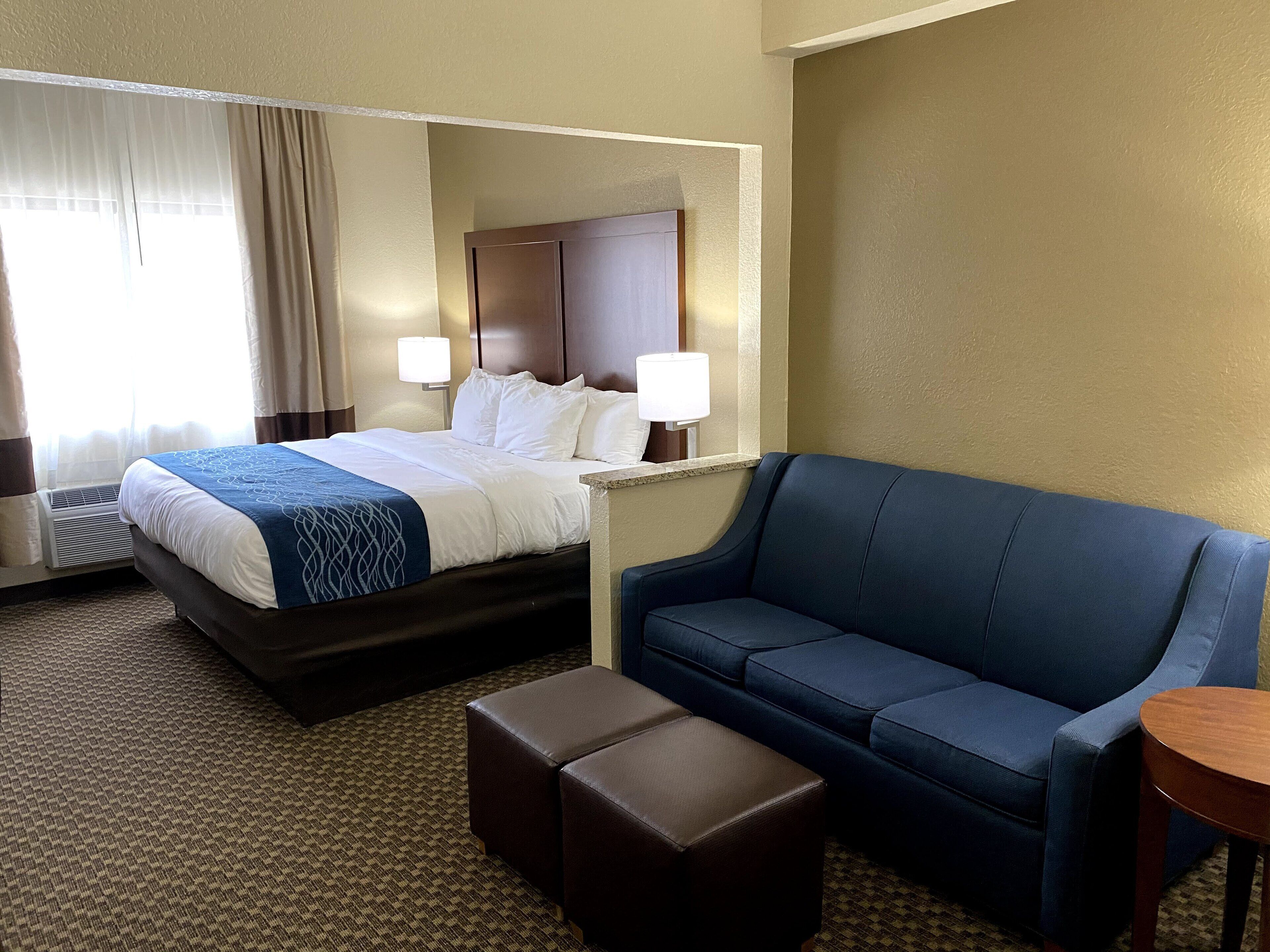 A hotel room with a bed, a blue sofa, an ottoman, and a small table.