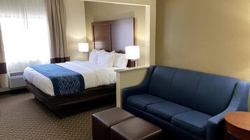 A hotel room with a bed, a blue sofa, an ottoman, and a small table.