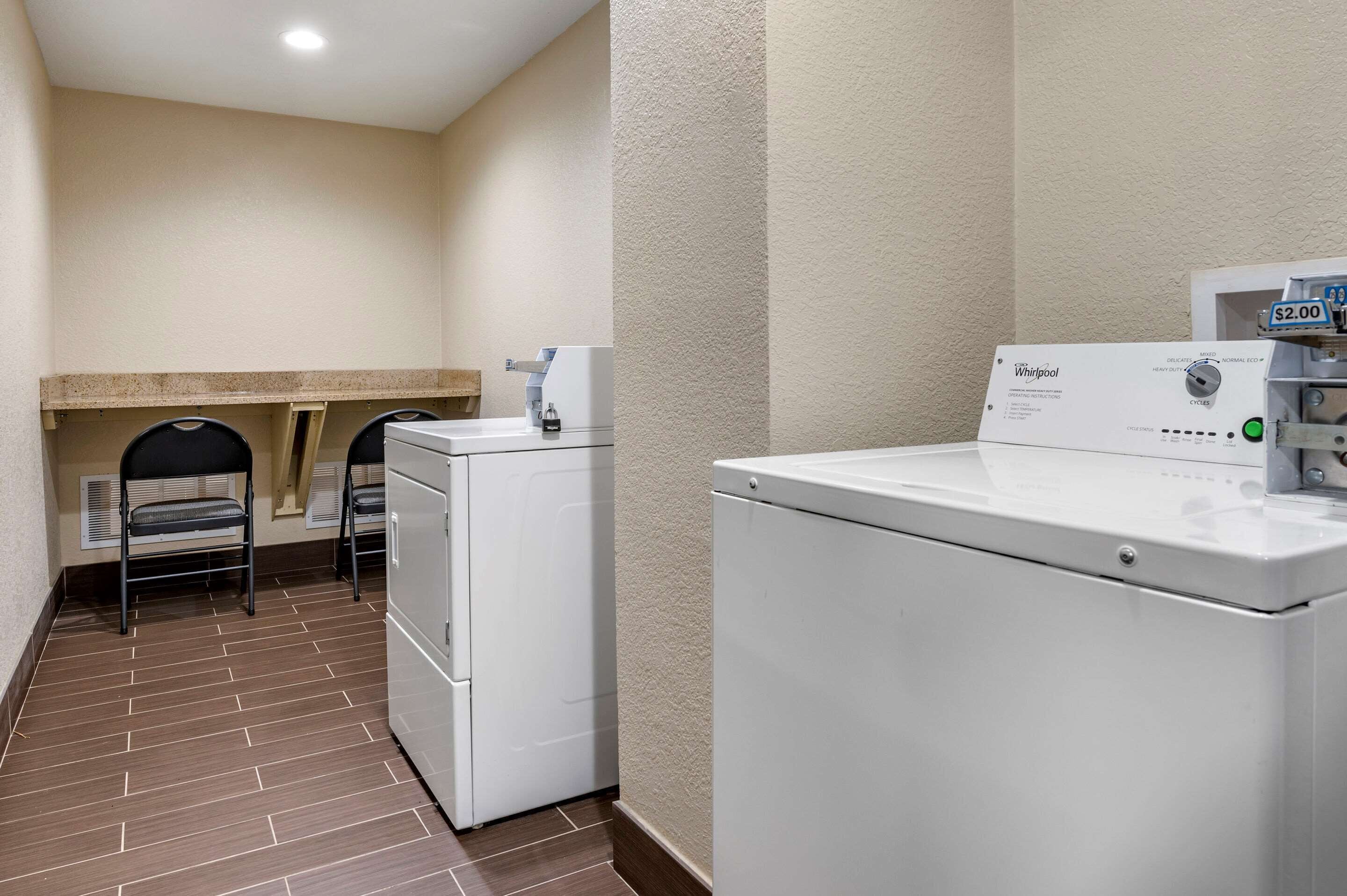 A laundry room with a Whirlpool washer and dryer, a small sink, and a chair.