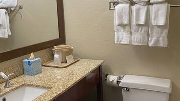 Un baño con lavamanos, espejo, toallero, inodoro y un cubo de basura.