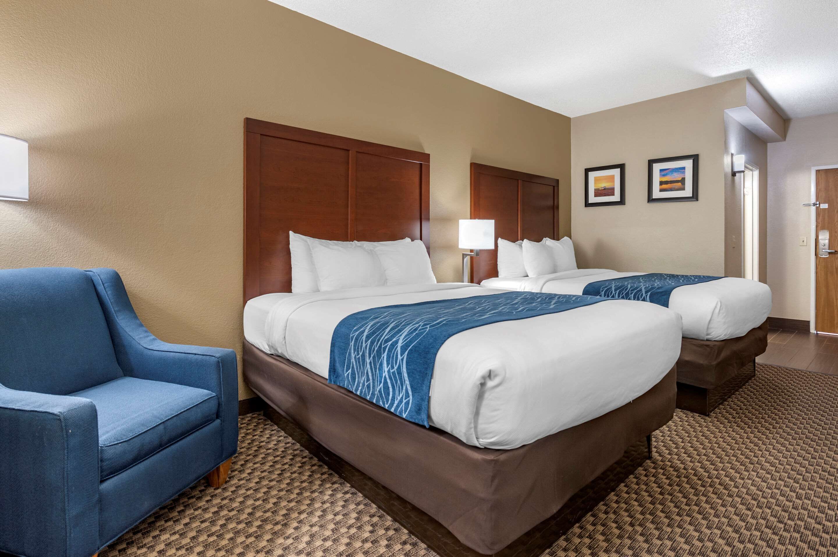 A hotel room with two beds, a blue armchair, and a patterned carpet.